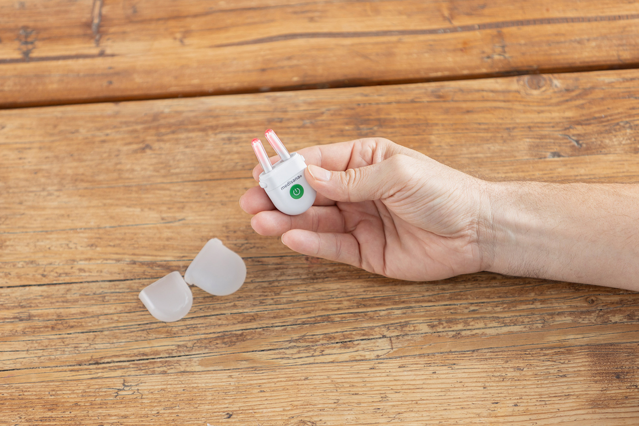 Hand hält dHand holding the medisana medinose compact with two interchangeable light attachments for allergy relief.ie medisana medinose compact, daneben liegen zwei Lichtaufsätze für die Anwendung gegen allergische Beschwerden.